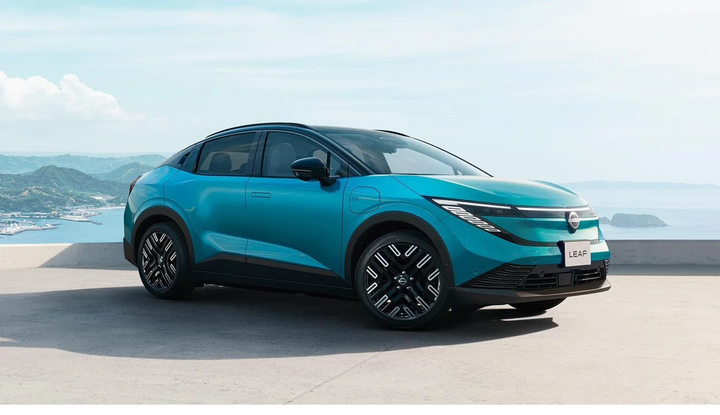 クロスオーバーSUVへ進化した日産リーフ(新型・ティールブルー)のフロントサイド外観。海と山を背景にした俯瞰イメージ